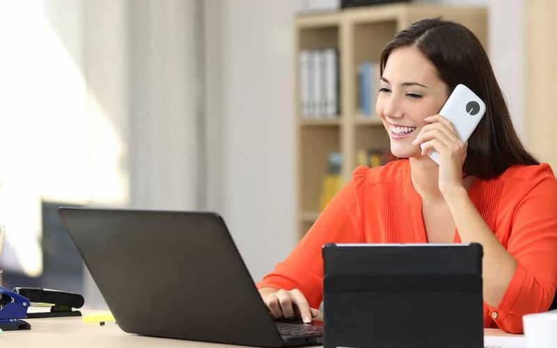 Cộng tác viên bất động sản sử dụng điện thoại và laptop để trao đổi công việc với khách hàng.